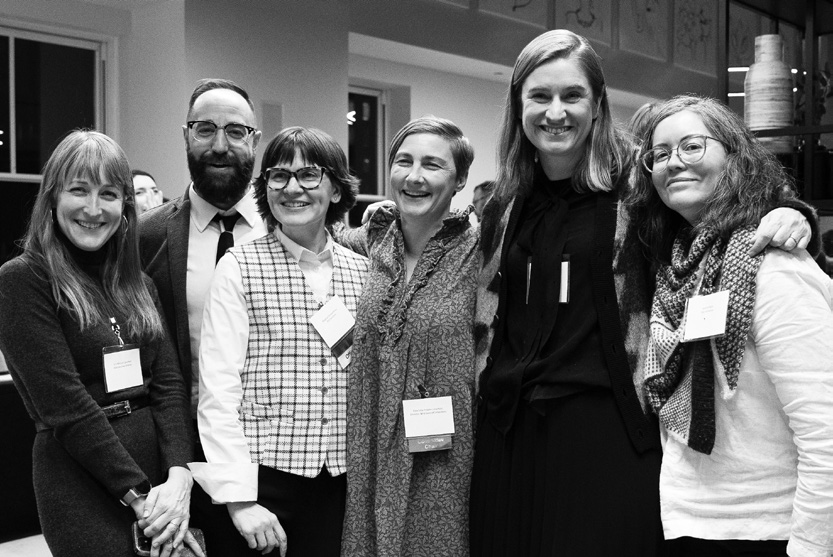 Black and white photo of a group of six people smiling at an indoor event.