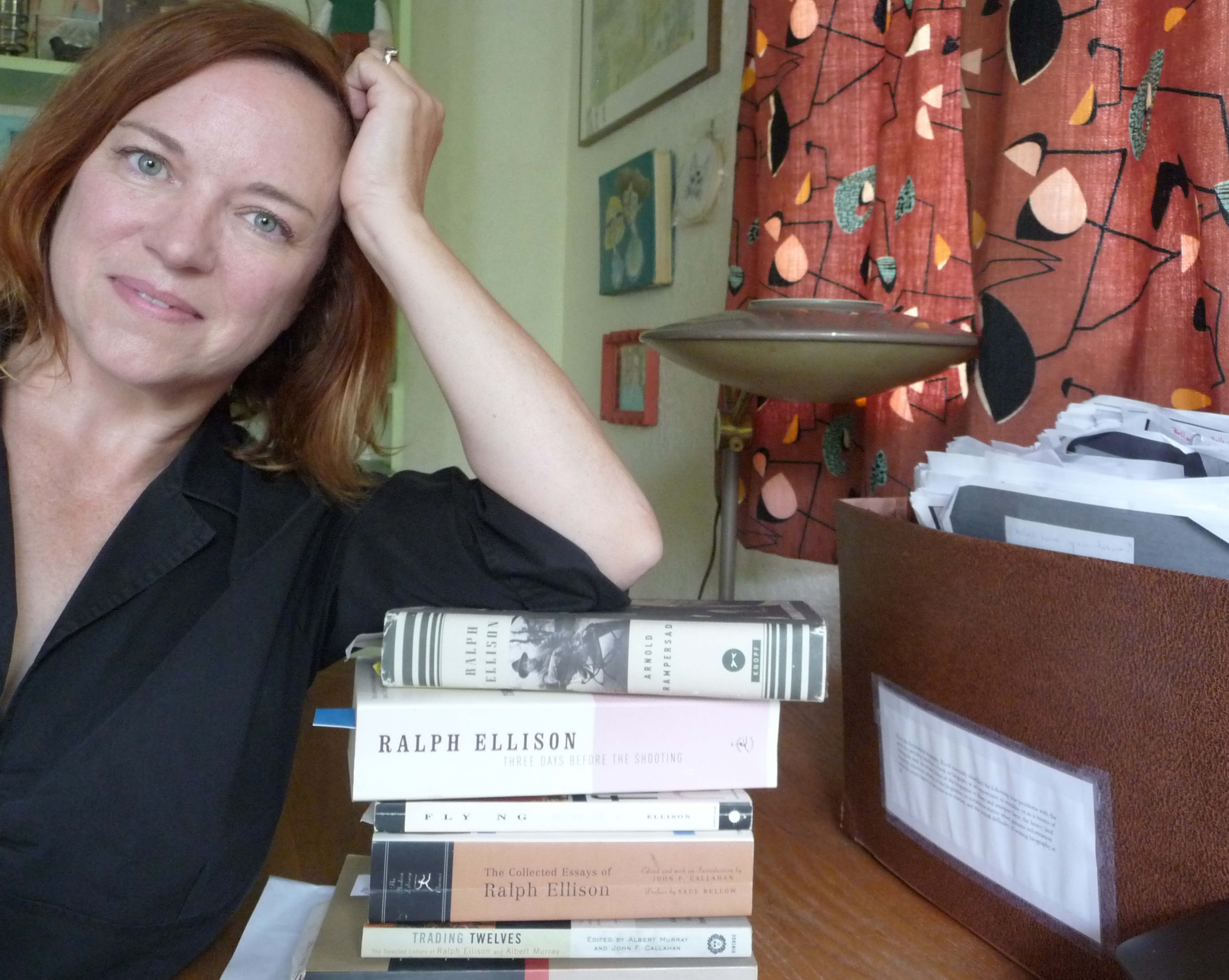 Tracy Floreani, wearing a black blouse, her head on her hand beside a stack of books by Ralph Ellison.