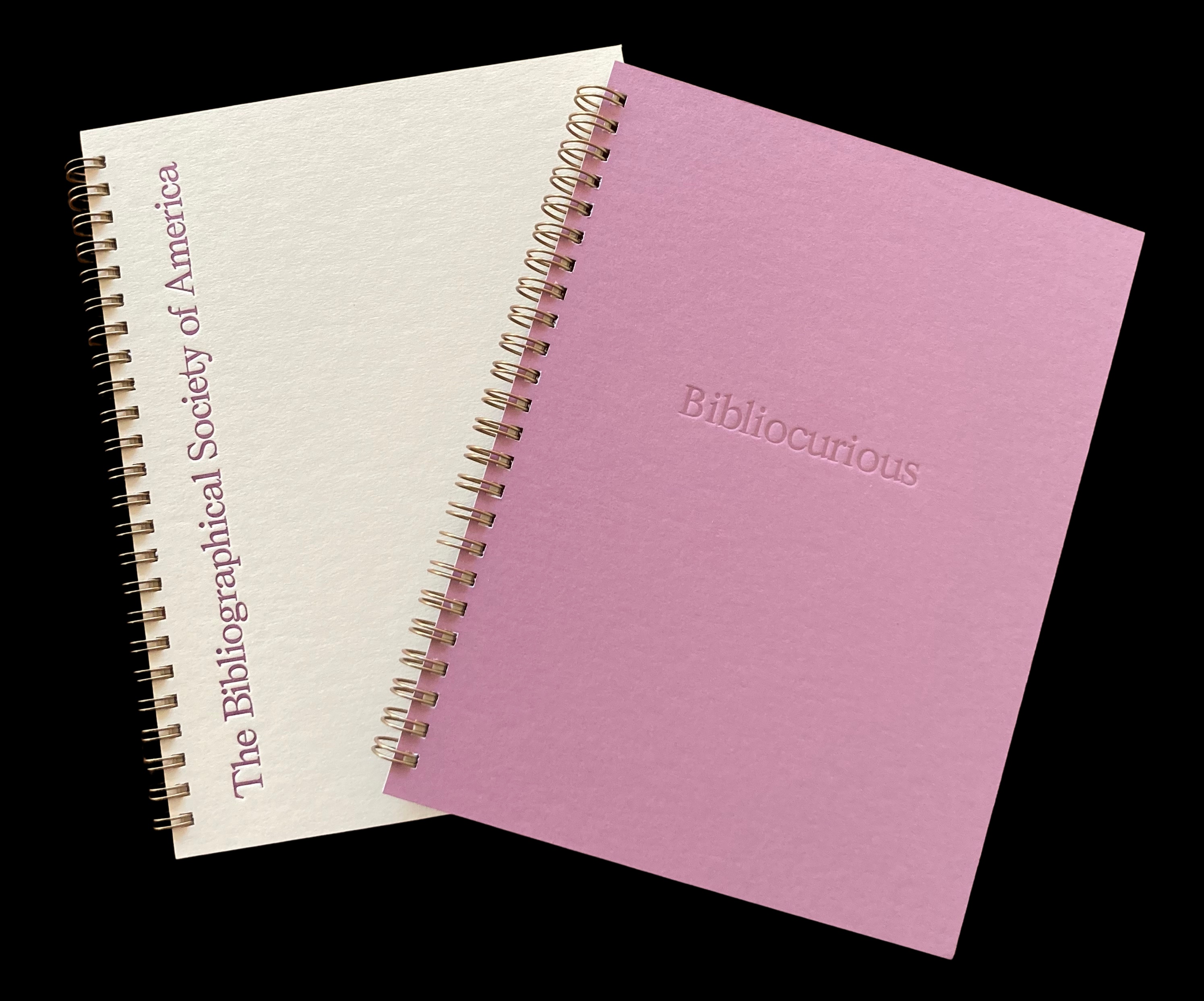 Two spiral-bound notebooks, one light purple and one cream-colored, with embossed and printed text.